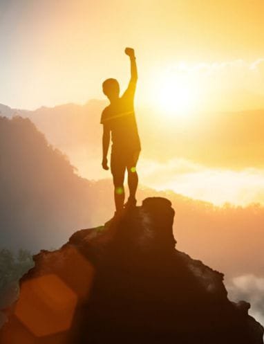 A Silhouette of a person standing on top of the mountain with sun in the background
